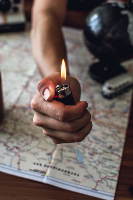 Close-up of a hand holding a lighter over a travel map, planning an adventure.