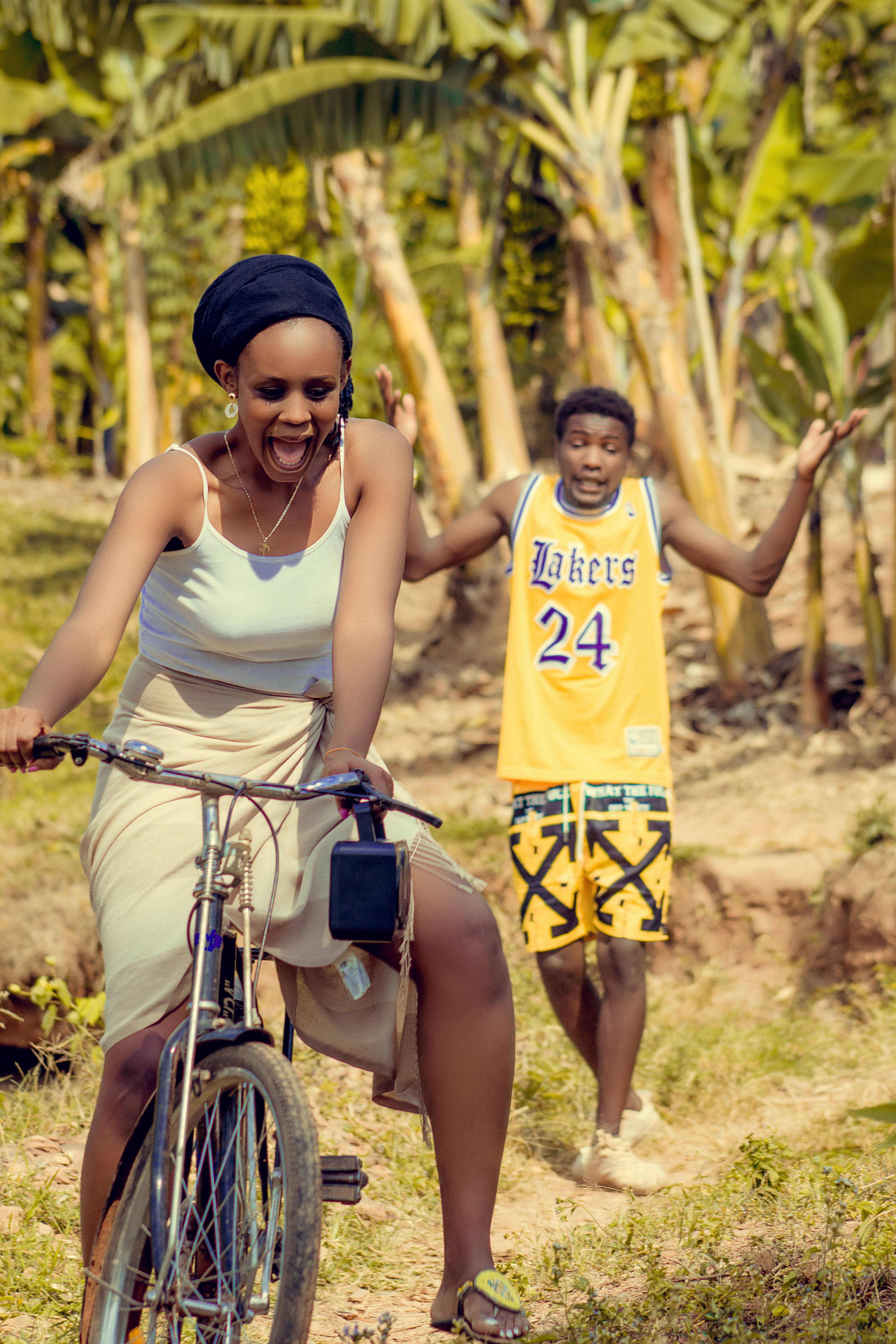 Laughing couple in Kigali enjoying a bike ride in a sunny outdoor setting.