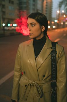 A fashionable woman in a leather coat gazing thoughtfully in an urban street at night.