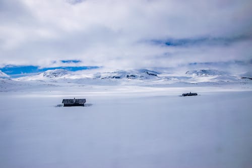 Ücretsiz Karla Kaplı Dağların Yakınında Bulutlu Gökyüzü Altında İki Ev Stok Fotoğraflar