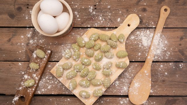Green spinach gnocchi on a paddle board with eggs, flour and a wooden spoon