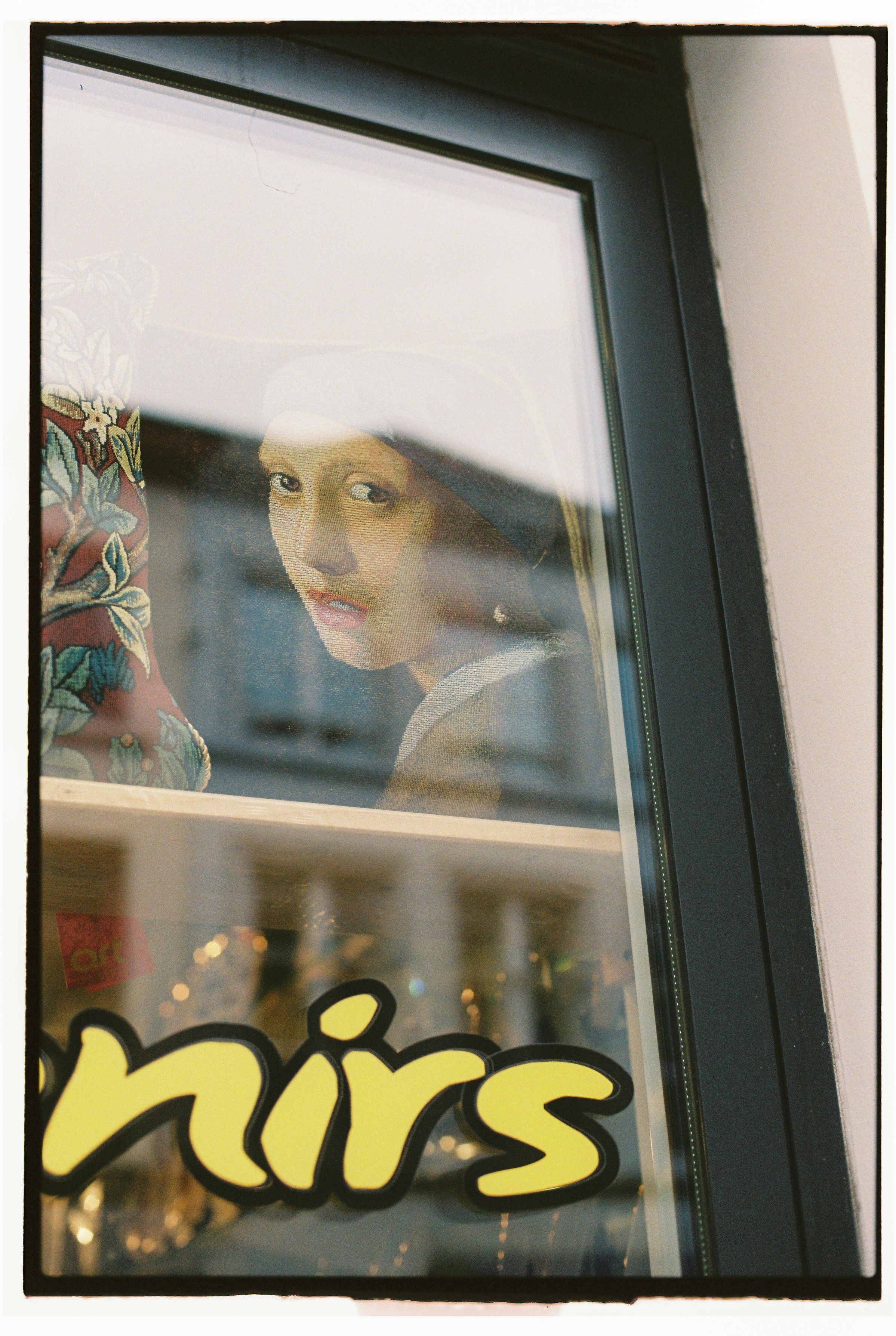 Creative reflection of Vermeer's 'Girl with a Pearl Earring' seen through a window in an urban setting.