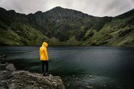在英国威尔士一个宁静的山湖边，站着一位穿着黄色雨衣的人