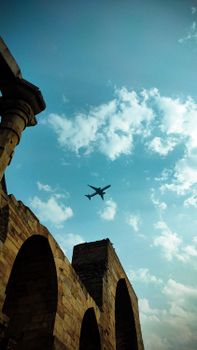 A low-angle view of an airplane flying over historic stone arches against a clear blue sky, capturing travel and architecture.