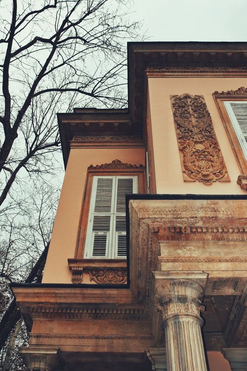 Free Low angle view of a historic house exterior with ornate columns and carvings against a leafless tree backdrop. Stock Photo