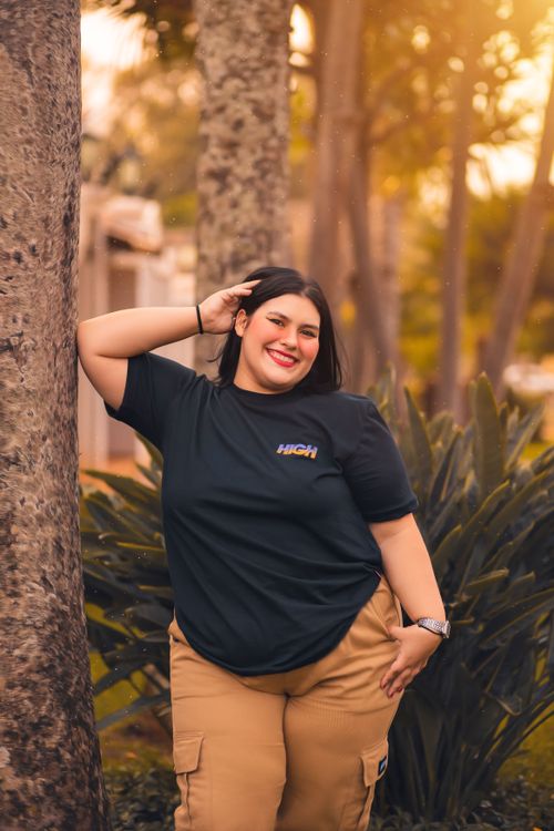 Free Smiling woman in a black t-shirt and cargo pants posing playfully outdoors among trees in Bauru, Brazil. Stock Photo