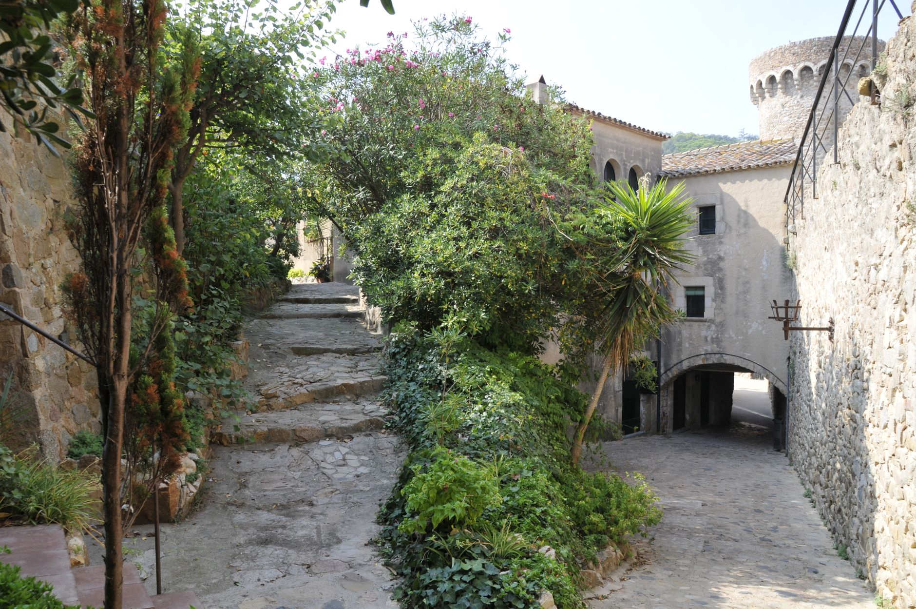 Cobbled lane inside the Vila Vella leading toward the Governor's House, with the sea visible through a gap between buildings