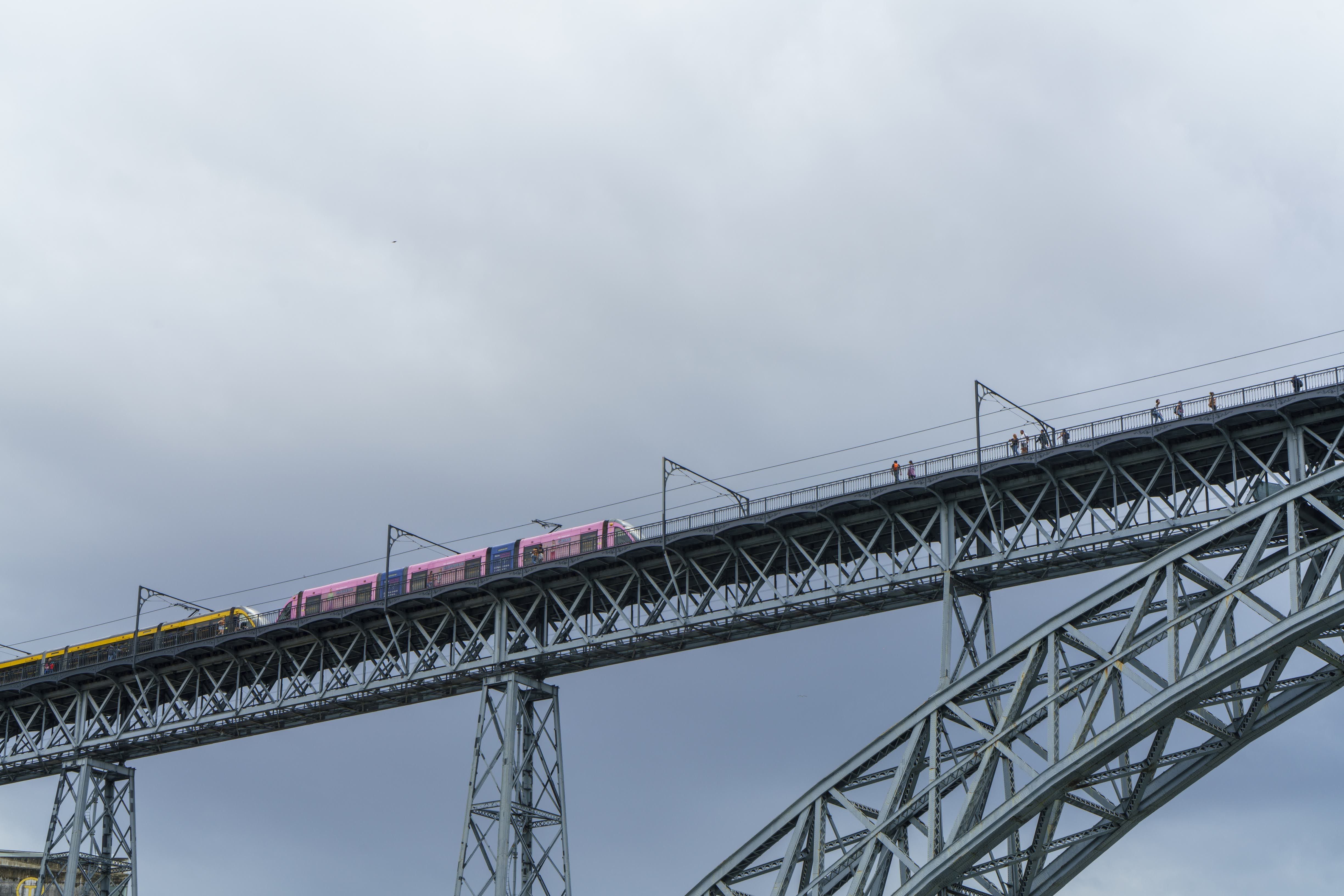 A colorful train crossing an iconic steel bridge with a cloudy sky backdrop, showcasing modern transportation.