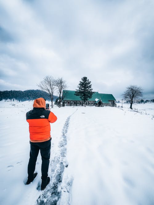  A Man in Orange and Black Jacket Standing on Snow Covered Ground