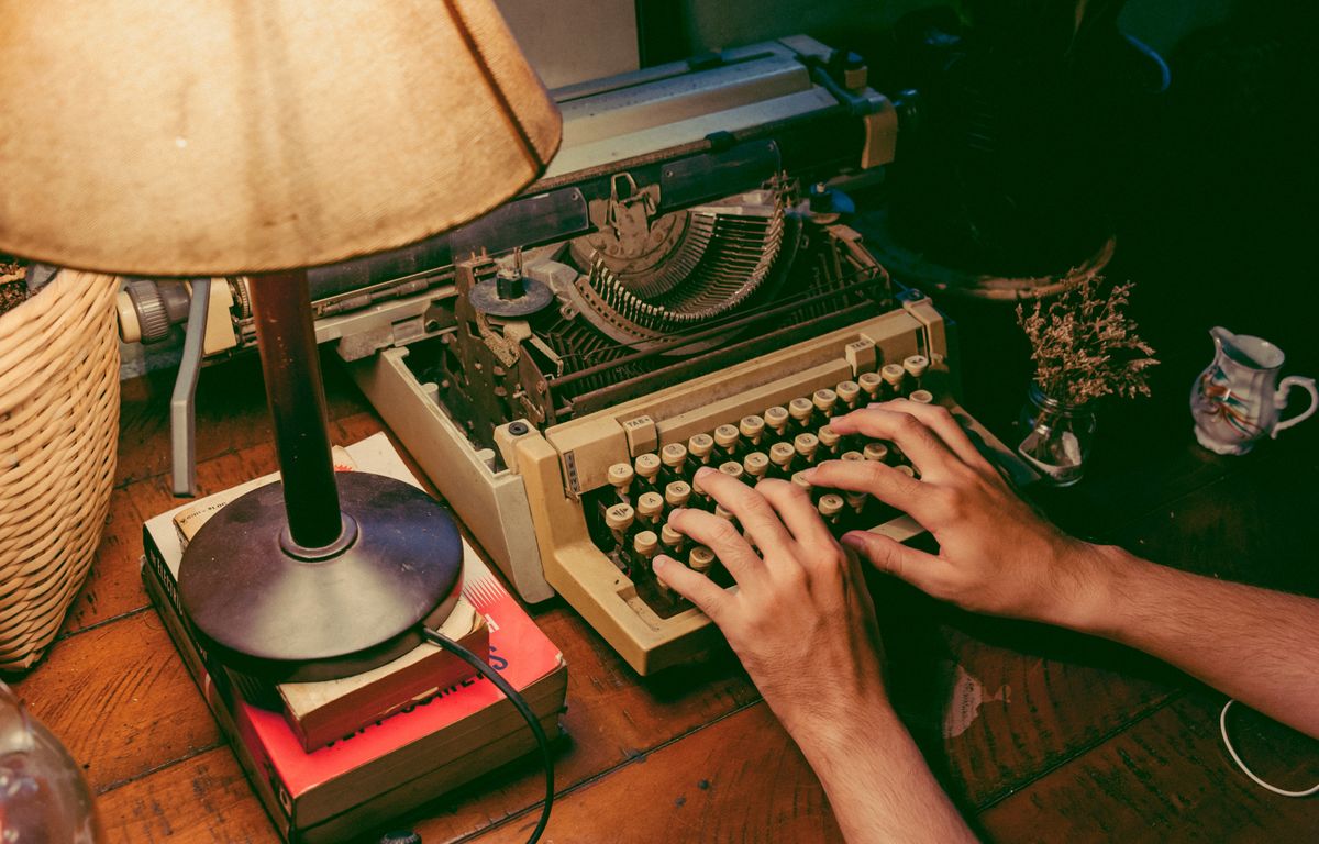 Hands typing on a vintage typewriter under a warm lamp — photo by Min An on Pexels