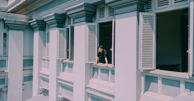 一名男子从一栋带有经典建筑风格和开放式百叶窗的历史建筑窗户探出身来