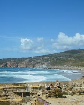 Stunning coastal beach scene with waves crashing against rocky cliffs under a bright blue sky.