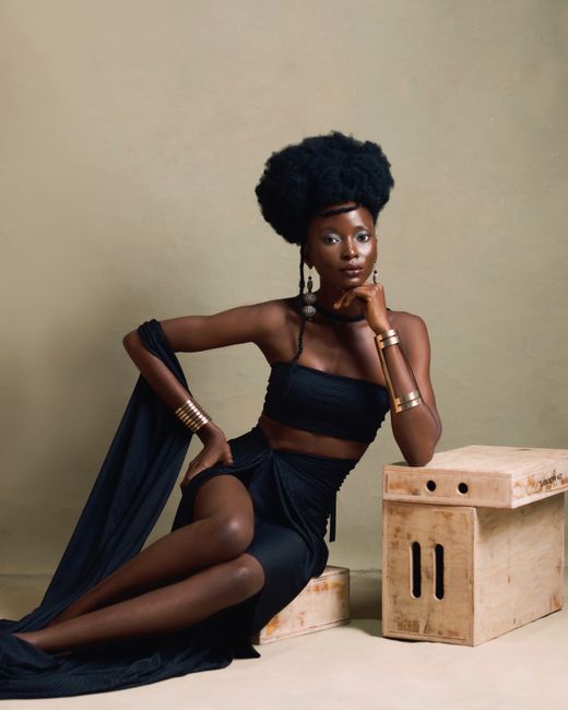 Stylish African woman with afro hair and elegant black attire posed in a studio setting.
