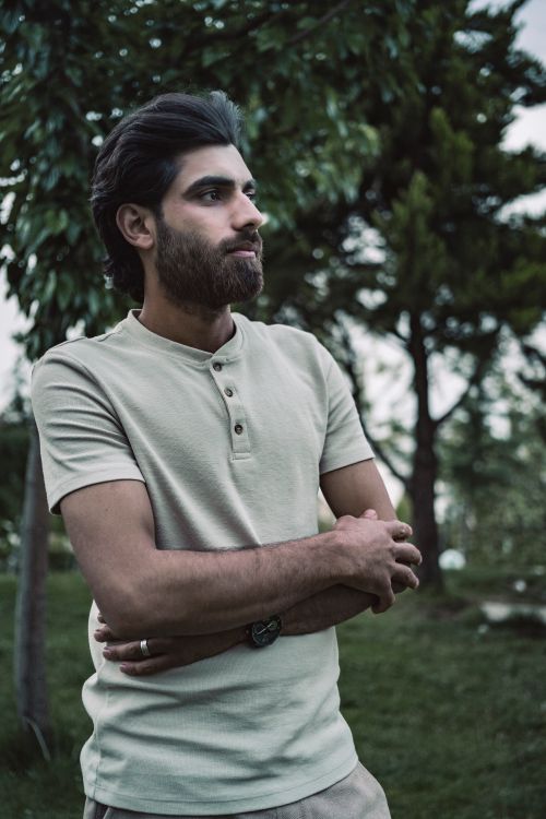 Free A serene portrait of a bearded man standing outdoors with arms crossed, in a lush green environment. Stock Photo