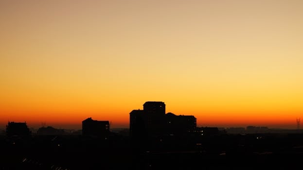 Silhouette of city buildings against a vivid orange sunrise sky.