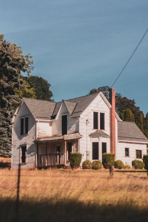 Free Rustic white farmhouse surrounded by autumn foliage under a clear blue sky. Stock Photo