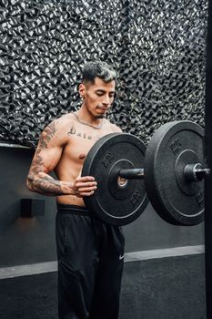 Shirtless tattooed man lifting weights, working out in a Mexico City gym.