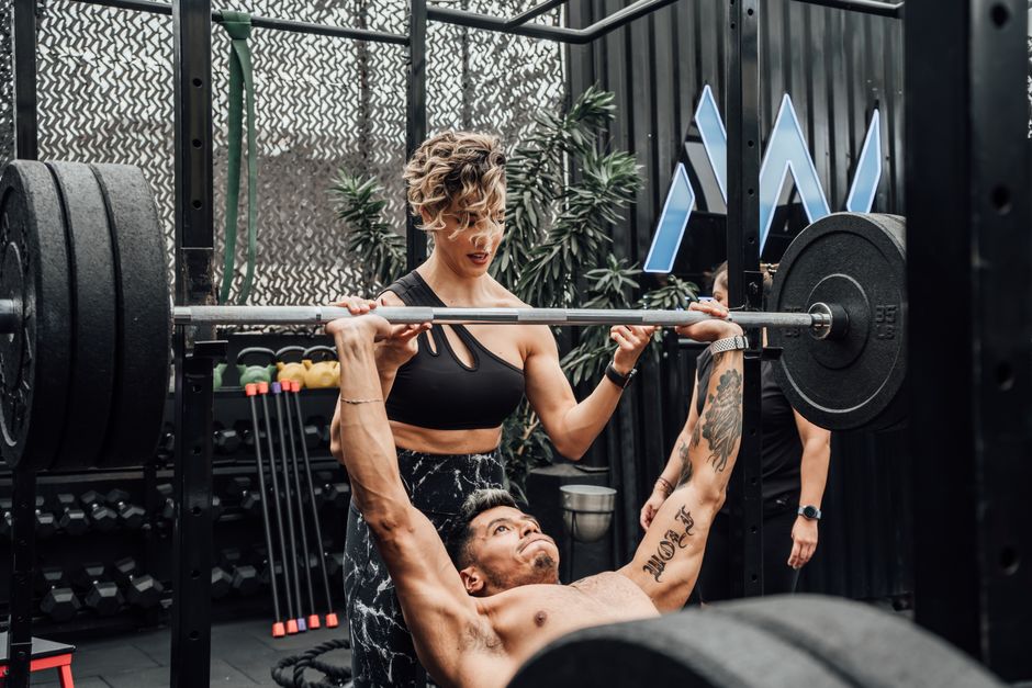 Man lifting weights with woman spotting in Mexico City gym. Urban and dynamic fitness scene.