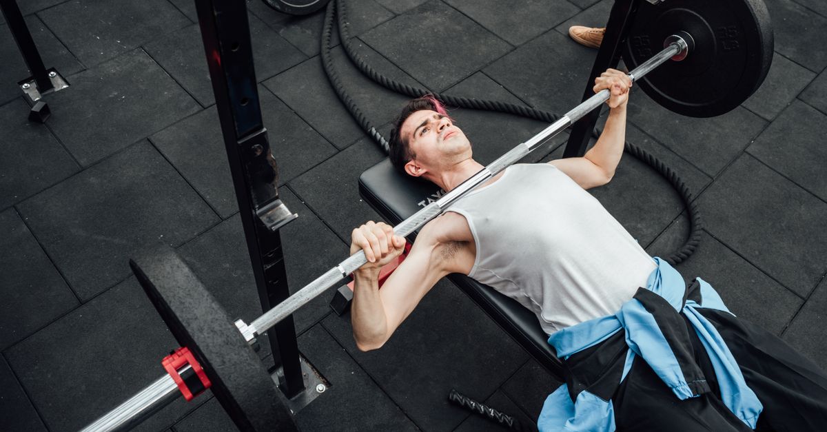 Adult male performing bench press in a Mexico City gym, showcasing strength training and fitness.