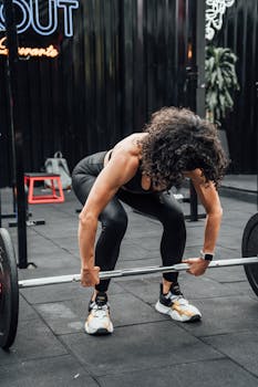A woman in activewear performing deadlifts with a barbell in a Mexico City gym.