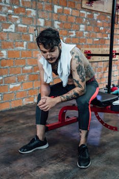 Exhausted athlete with tattoos taking a break on a gym bench indoors in Mexico City.