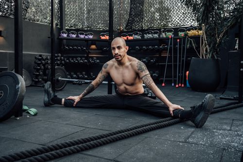 Free Tattooed man performing a split stretch in a gym, showcasing flexibility and fitness lifestyle in Mexico City. Stock Photo