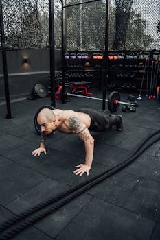Shirtless tattooed man performing push-ups on gym floor in Mexico City, showcasing fitness and strength.