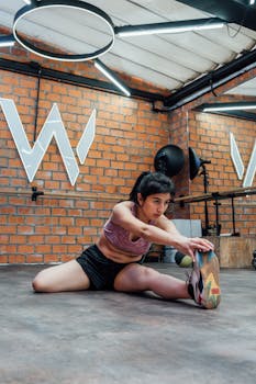 Woman in activewear doing stretches in an urban gym with exposed brick walls.