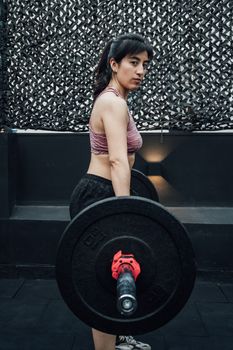 Female athlete lifting barbell indoors, showcasing strength and fitness in a gym setting.