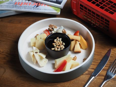 A stylish cheese platter featuring assorted cheeses, nuts, and strawberries on a wooden table.