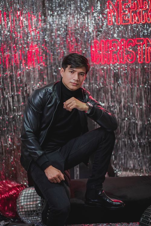 Free Fashionable man kneeling in a festive Christmas-themed backdrop, exuding confidence and style. Stock Photo