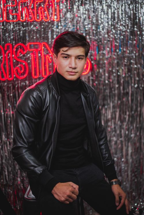 Free Young man posing confidently in a festive studio with Christmas decorations and glittering backdrop. Stock Photo