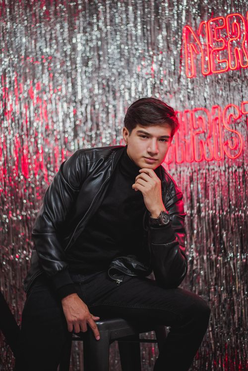 Free Young man in black leather jacket posing against festive glitter backdrop for Christmas. Stock Photo