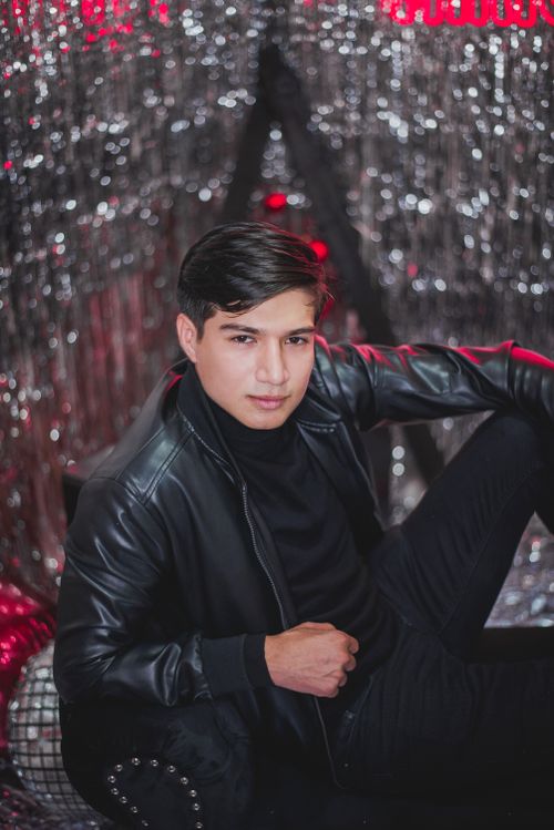 Free Young man in black leather jacket posing with sequins backdrop, creating a fashionable look. Stock Photo