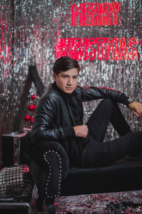 Free Young man in leather jacket posing confidently in a decorated Christmas studio setting. Stock Photo
