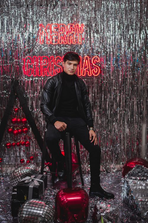 Free Young man sitting in a festive Christmas setting with glittering decorations and gifts. Stock Photo