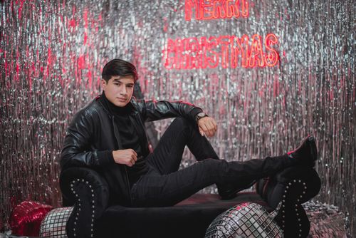 Free Man posing on a couch in a modern Christmas-themed studio with metallic decor. Stock Photo