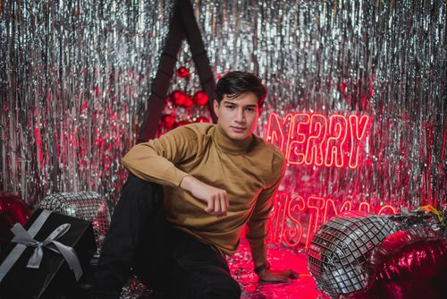 Free Young man poses in a festive setting with Christmas decorations and a Merry Christmas sign. Stock Photo