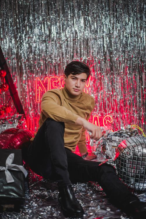 Free A stylish man in a turtleneck sits amidst festive decorations with a Merry Christmas sign. Stock Photo