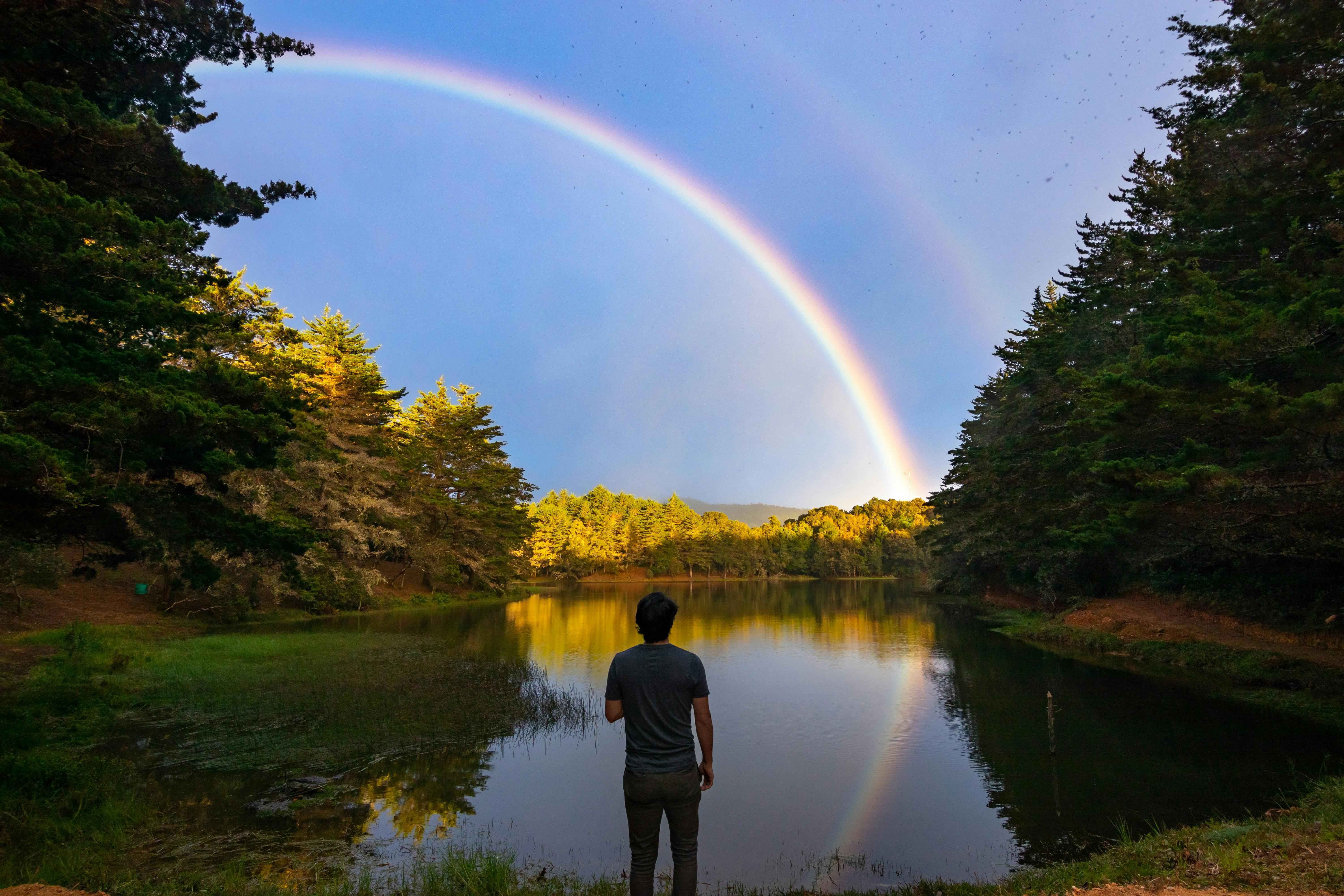 A man admires a stunning rainbow over a serene lake in El Jardín, Costa Rica.