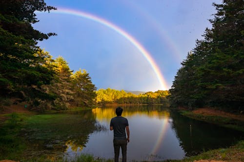 Free Man Standing by the Lake and Looking at the Rainbow Stock Photo