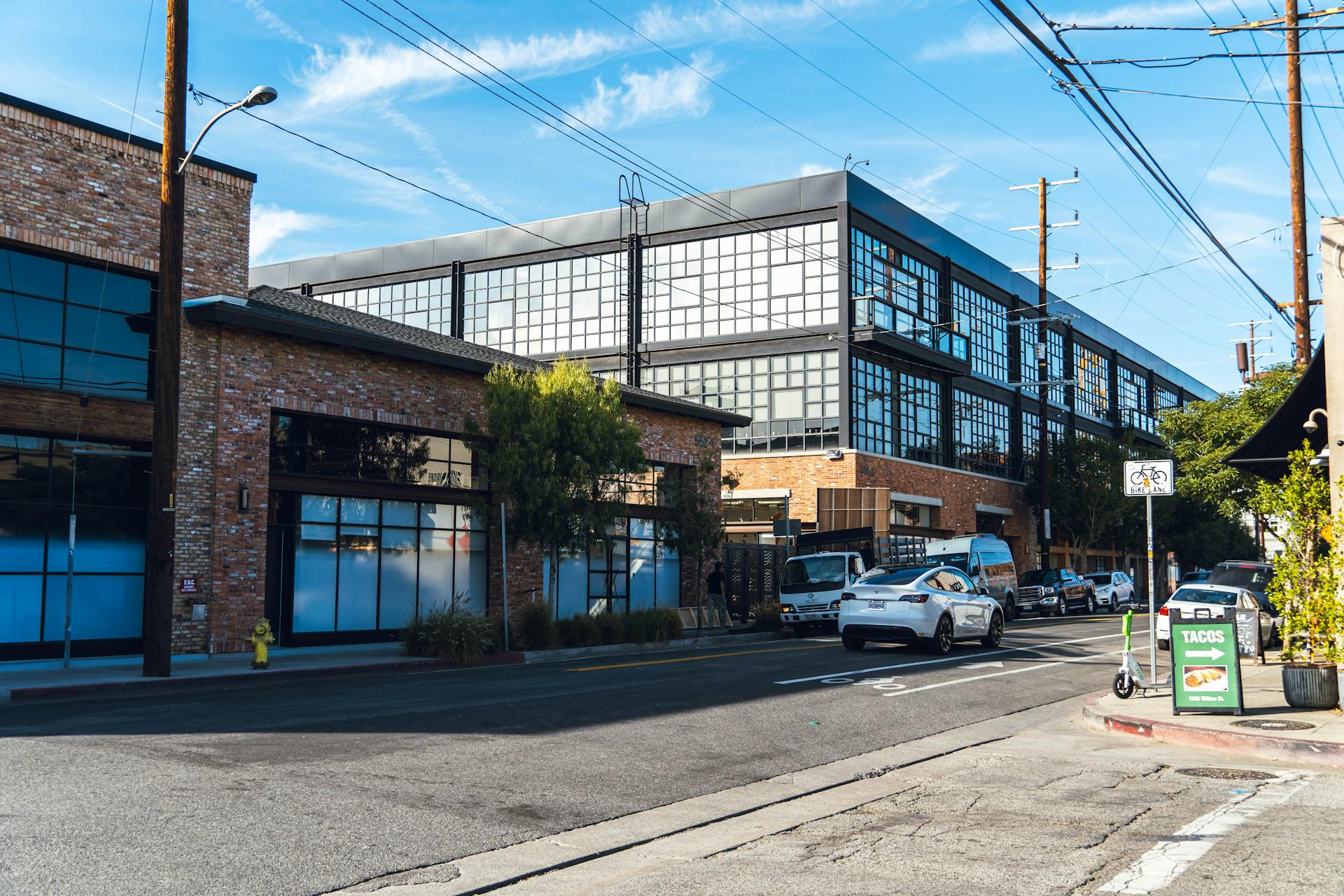 A busy street in LA featuring modern industrial warehouses under a clear blue sky.