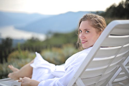 Free Selective Focus Photography of Smiling Woman Wearing White Bathrobe Lying on Pool Chair Stock Photo