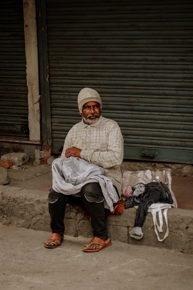 Man Sitting On The Street Beside His Clothes 