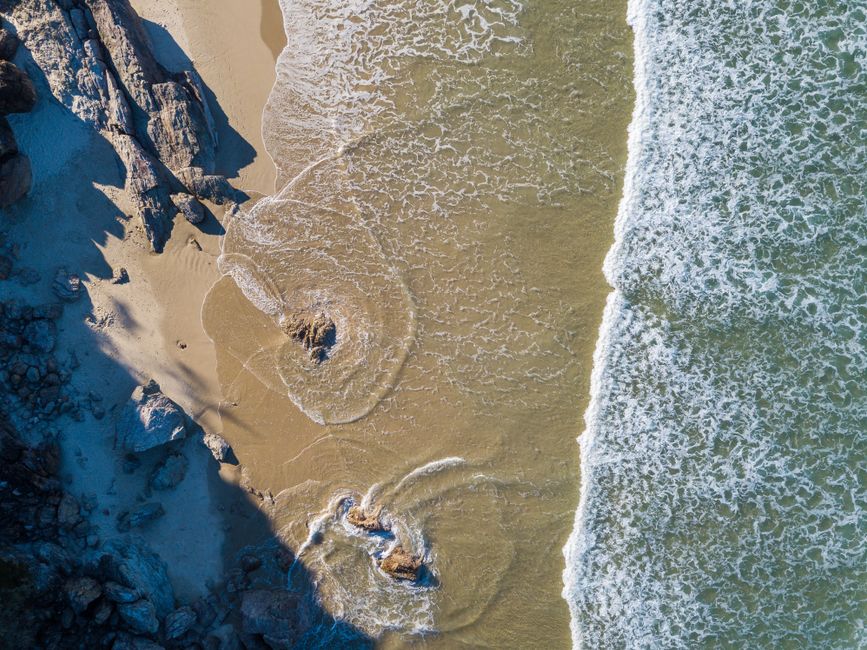 Drone view of waves hitting the sandy shore in Newcastle East, Australia.