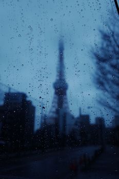 Blurred Tokyo Tower seen through rain-covered window, creating a moody urban scene.