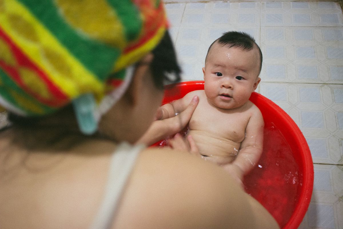 Mother gently bathing her baby in a small tub