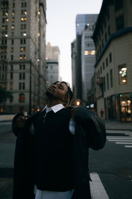 Man poses elegantly in a suit amidst modern architecture in a city during dusk.