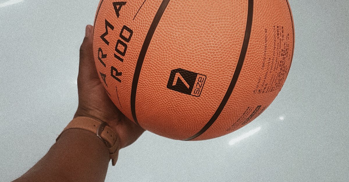 A hand gripping an orange basketball indoors showing the texture and detail.
