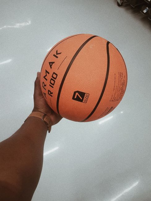 A hand gripping an orange basketball indoors showing the texture and detail.